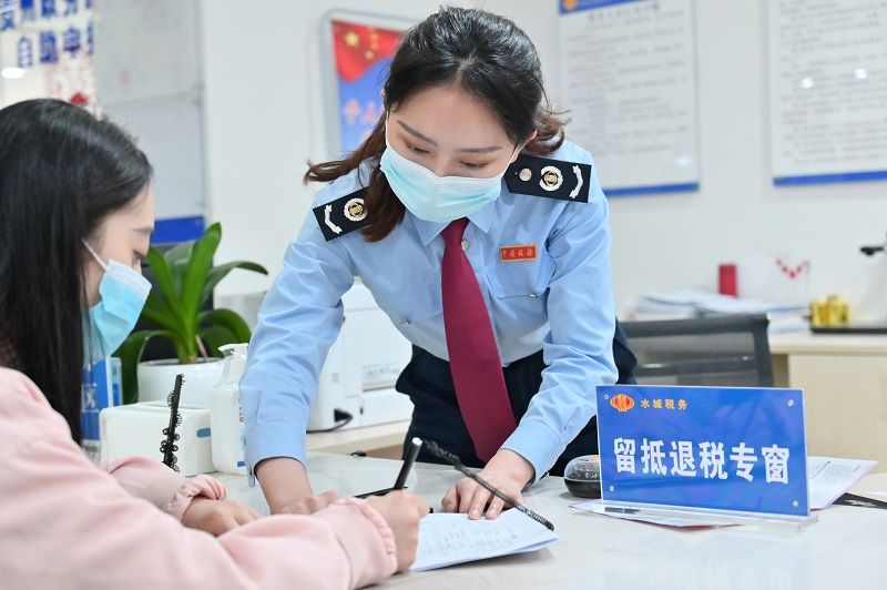水城區稅務局窗口工作人員正在輔導納稅人填寫資料。（張定國攝）.jpg